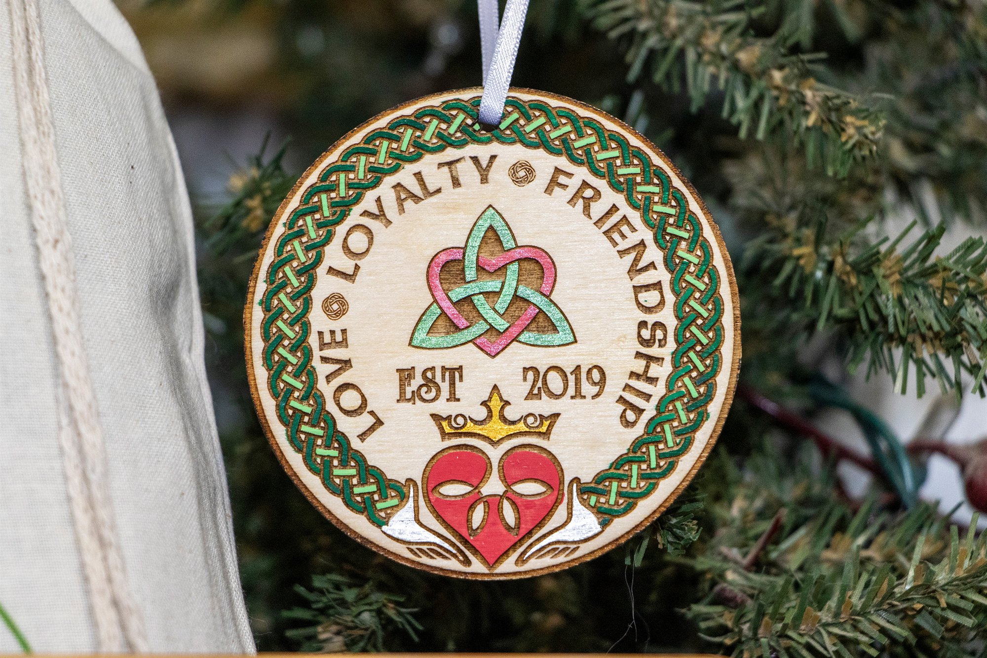 Round ornament with a Claddagh heart and the words Love, Loyalty, Friendship, hanging on a Christmas tree