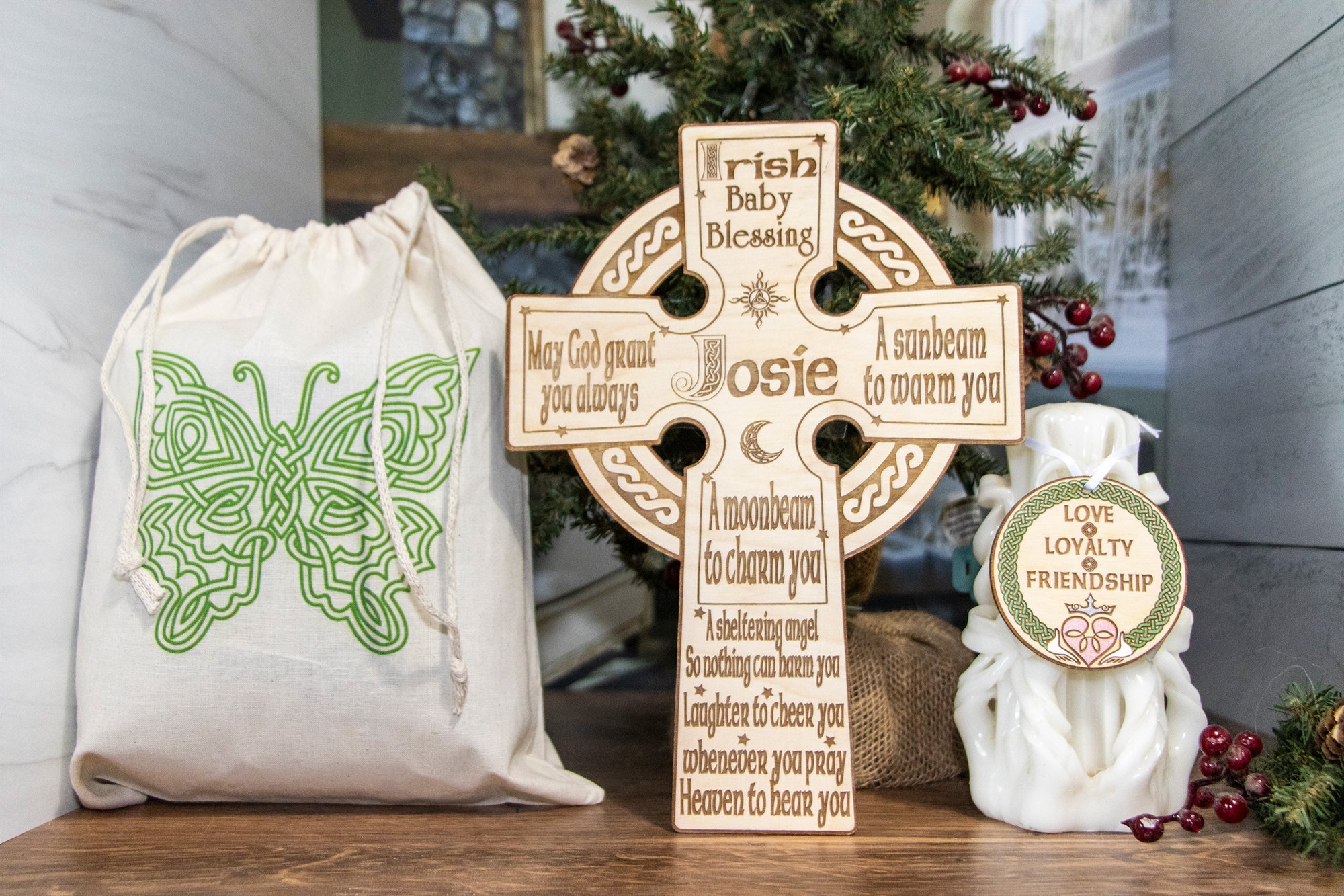 Wooden cross engraved with an Irish baby blessing and a child’s name, beside a gift bag
