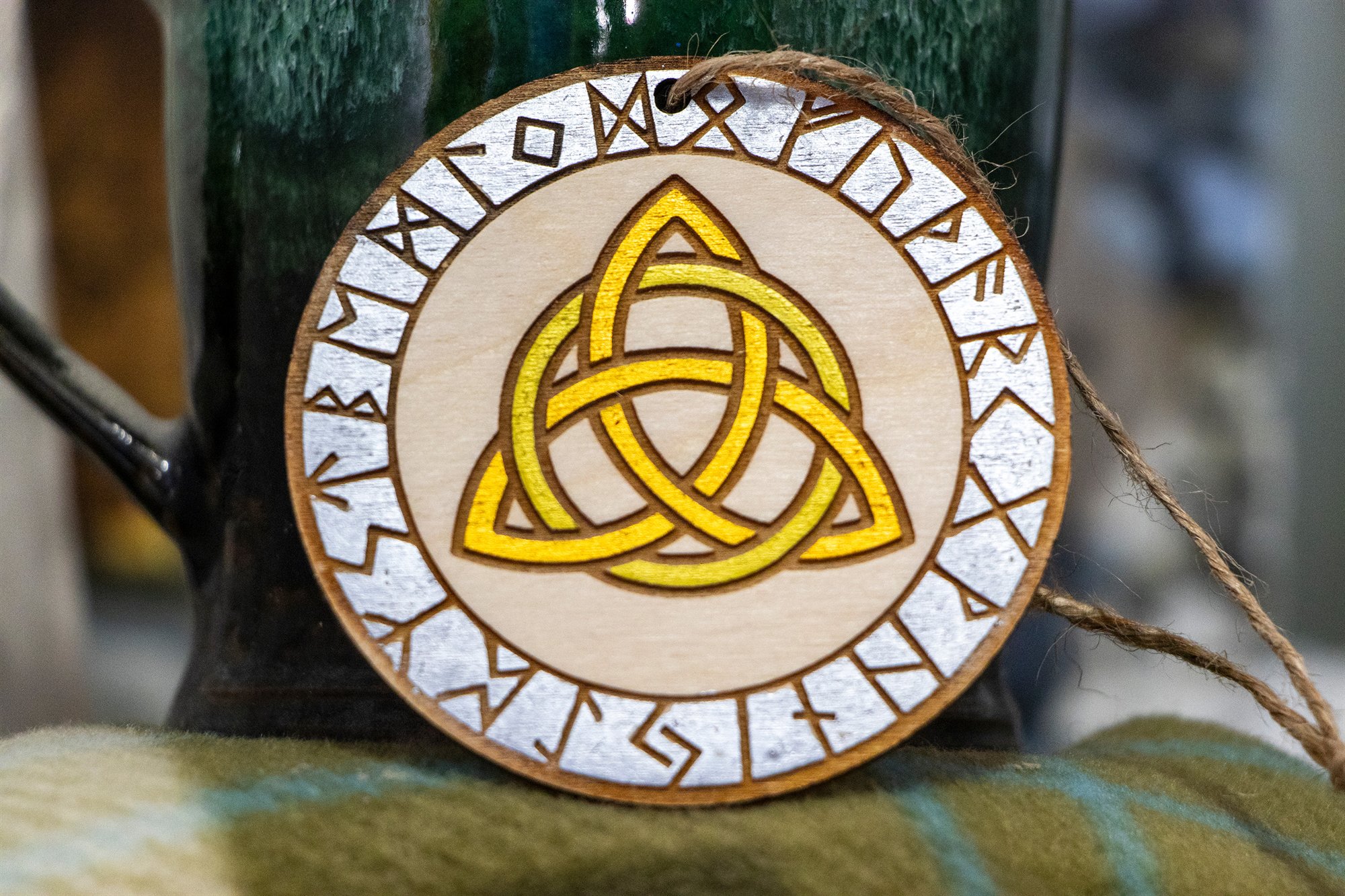 Round wooden ornament with a gold triquetra inside a ring of engraved runes